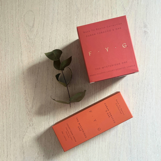 FYG Cuban Tobacco & Oak candle, beside the matching luxury hand cream on a wooden table.
