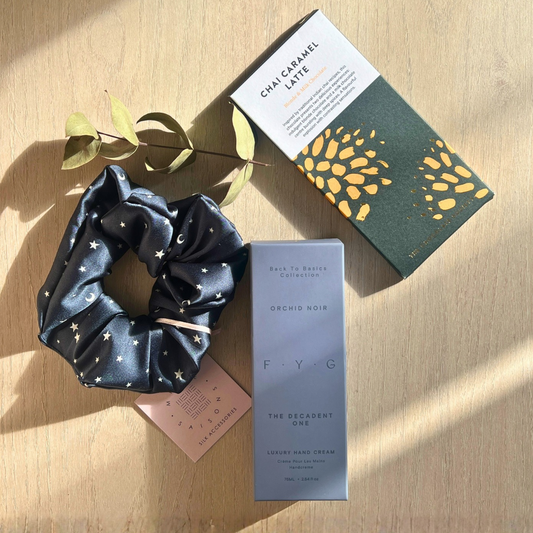 Navy star print silk scrunchie, FYG Orchid Noir hand cream and a chai caramel chocolate bar arranged together as a self-care gift set.