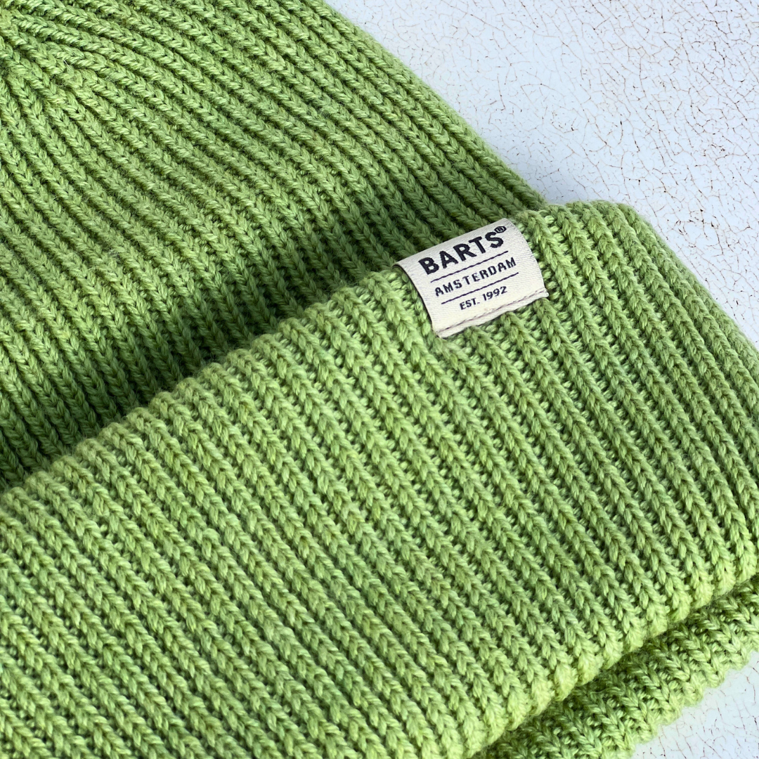 A close-up of a light green ribbed knit beanie hat with a folded cuff, featuring a white rectangular BARTS Amsterdam label.